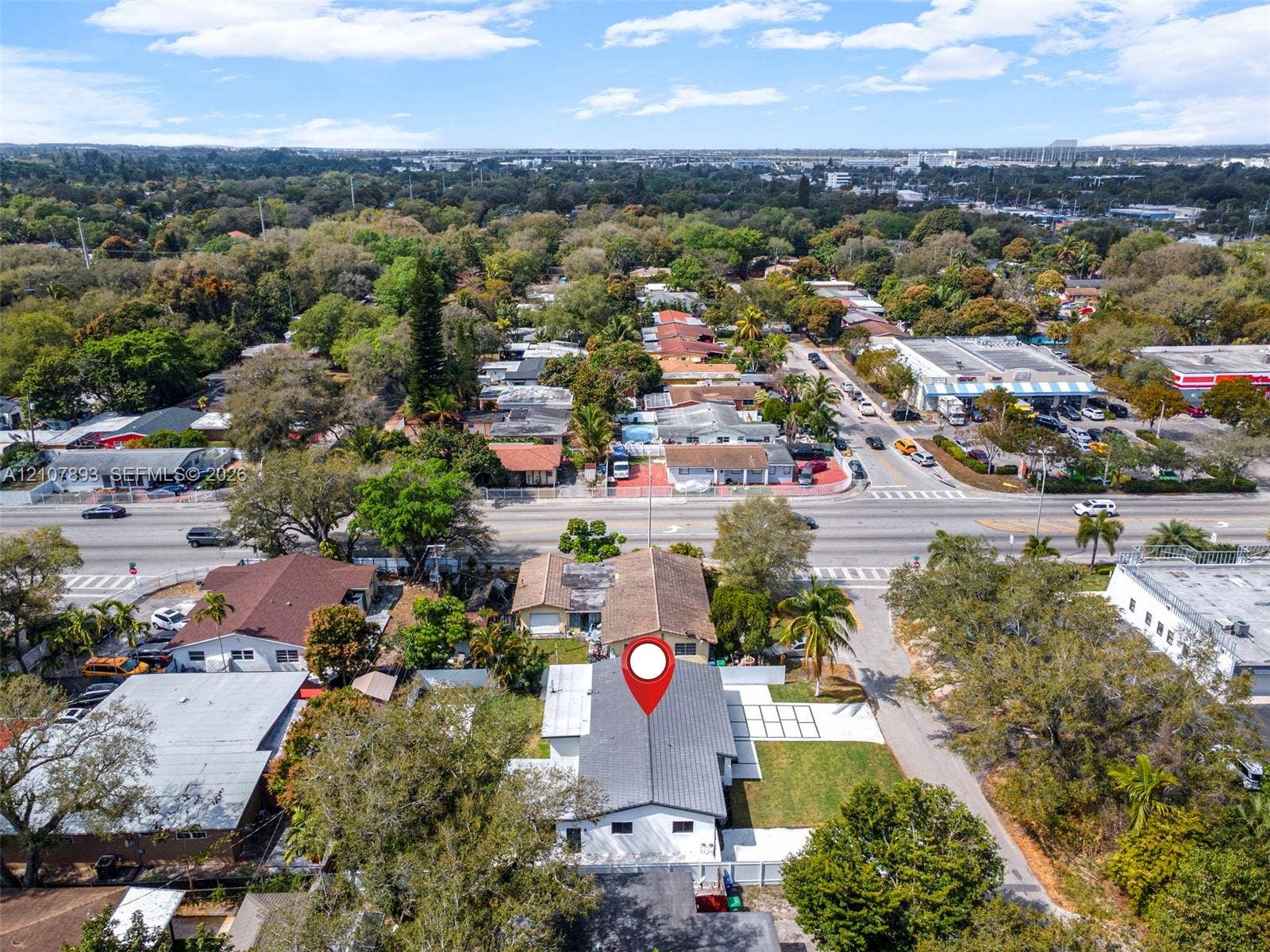 610 NE 164th Terrace, Miami, FL 33162 Aerial perspective featuring a multi-pitched shingle roof, white exterior finish, and a paved grid-patterned driveway