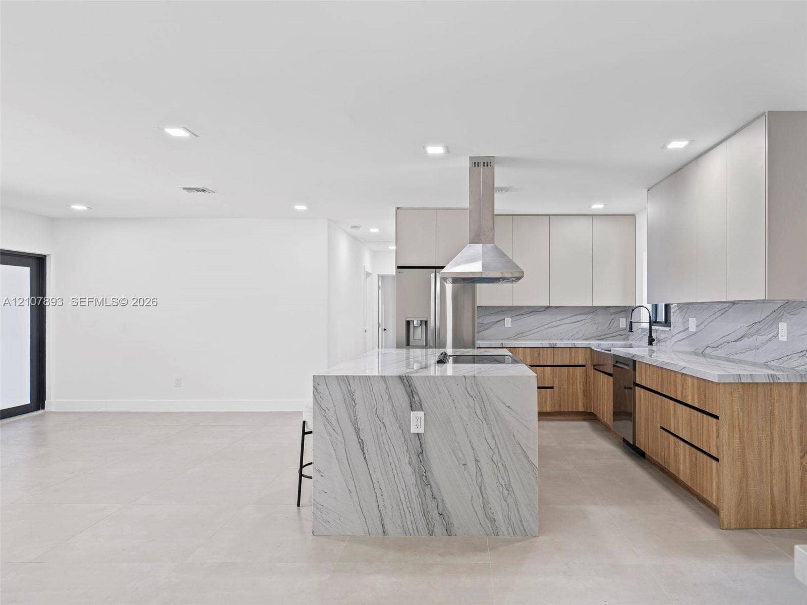 610 NE 164th Terrace, Miami, FL 33162 Modern kitchen featuring flat-panel cabinetry, stone-patterned countertops with matching waterfall island, stainless steel range hood, and large-format tile flooring