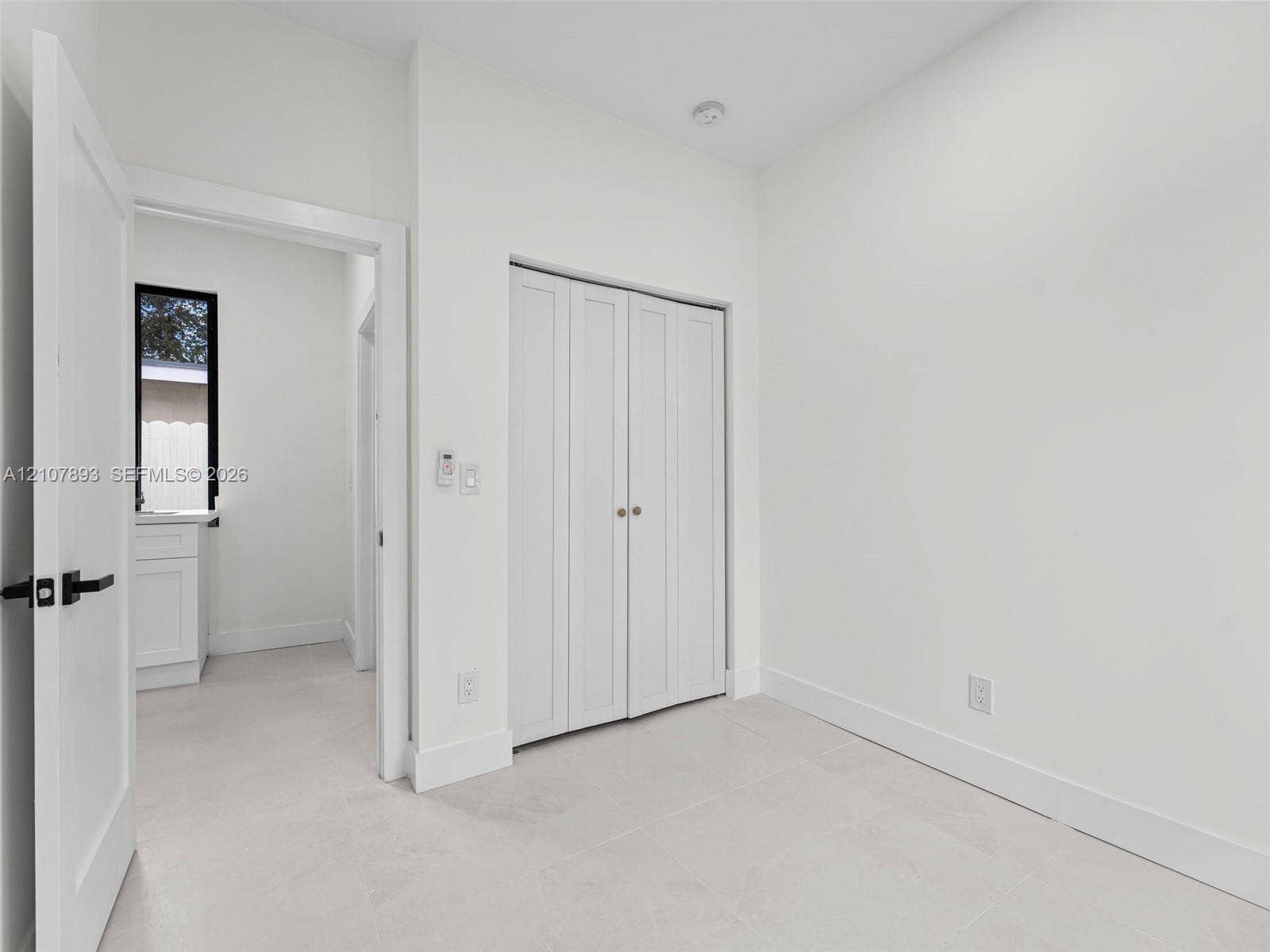 610 NE 164th Terrace, Miami, FL 33162 Neutral-toned interior featuring crisp white walls, tile flooring, and white bifold closet doors with metallic hardware