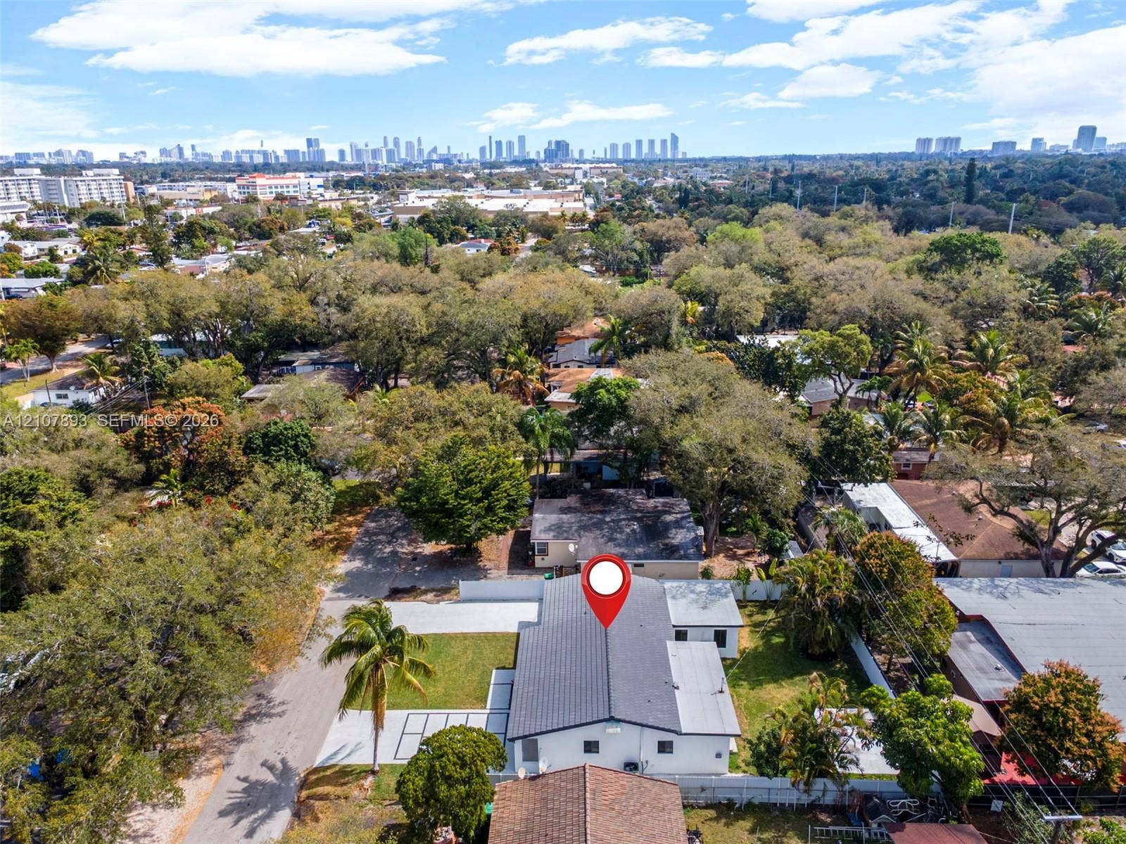 610 NE 164th Terrace, Miami, FL 33162 Aerial perspective featuring a detached residential property with a shingle roof, paved driveway, landscaped grounds with mature trees, and a perimeter fence