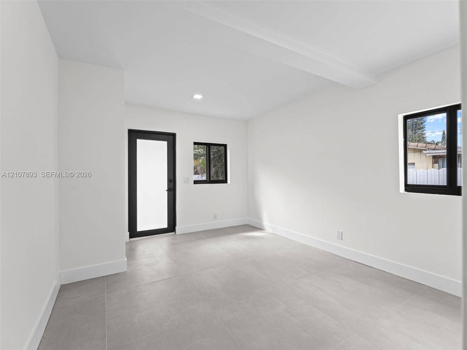 610 NE 164th Terrace, Miami, FL 33162 Neutral interior space featuring large-format tile flooring, matte black window and door frames, and flush-mount recessed lighting