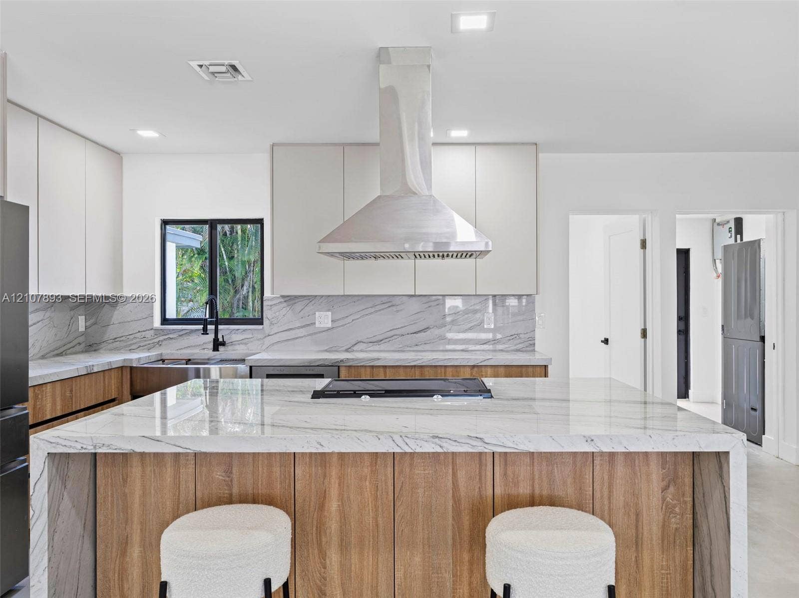 610 NE 164th Terrace, Miami, FL 33162 Kitchen featuring a waterfall-edge stone island with a cooktop, wood-finish cabinetry, stone slab backsplash, stainless steel chimney range hood, and matte black faucet