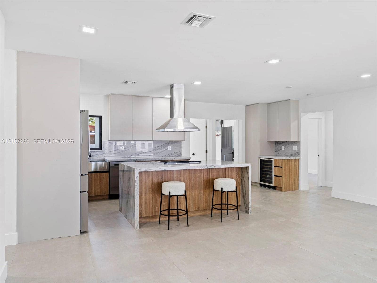 610 NE 164th Terrace, Miami, FL 33162 Kitchen featuring flat-panel cabinetry, a waterfall-edge stone island, stainless steel range hood, built-in wine refrigerator, and tile flooring