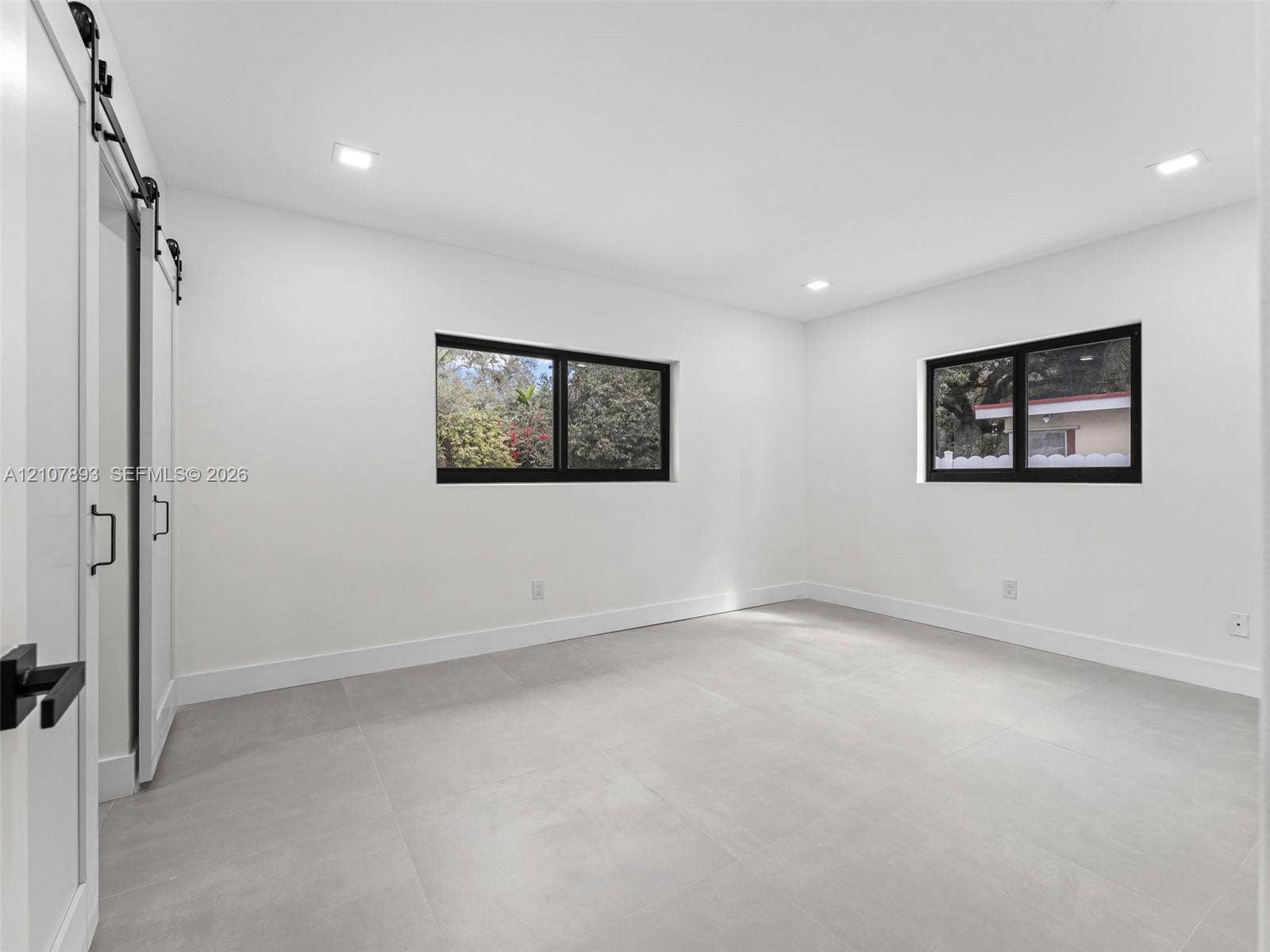 610 NE 164th Terrace, Miami, FL 33162 Interior space featuring neutral large-format tile flooring, recessed lighting, dual-pane windows with black frames, and a white sliding barn door with matte black hardware