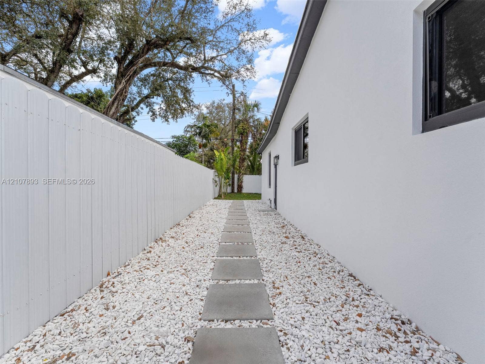 610 NE 164th Terrace, Miami, FL 33162 Side yard featuring a concrete paver walkway, white rock ground cover, and a solid white privacy fence