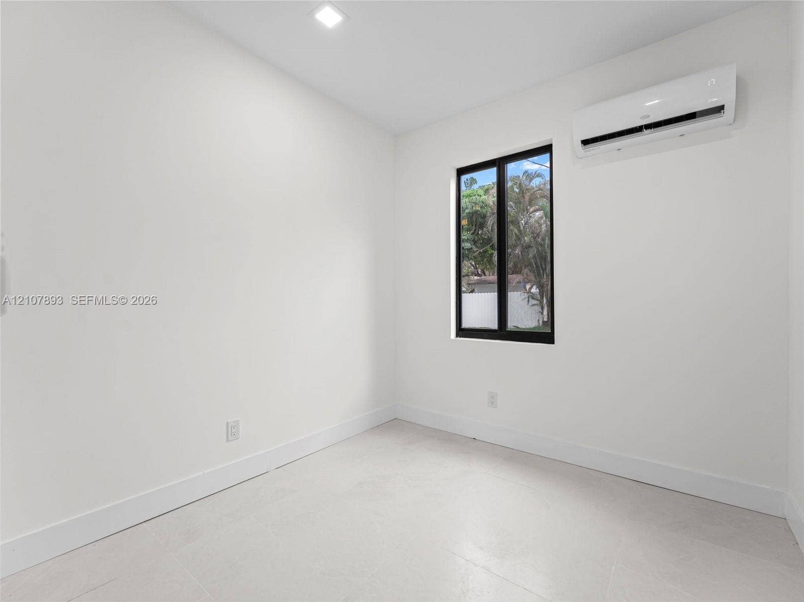 610 NE 164th Terrace, Miami, FL 33162 Interior space featuring white walls, light-colored tile flooring, a wall-mounted ductless air conditioning unit, recessed lighting, and a single window with a black frame