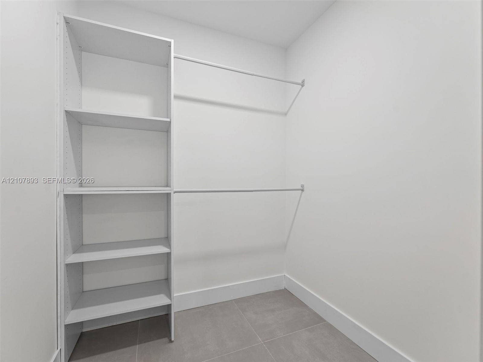 610 NE 164th Terrace, Miami, FL 33162 Walk-in closet featuring white built-in shelving and dual-tier metal hanging rods with neutral tile flooring