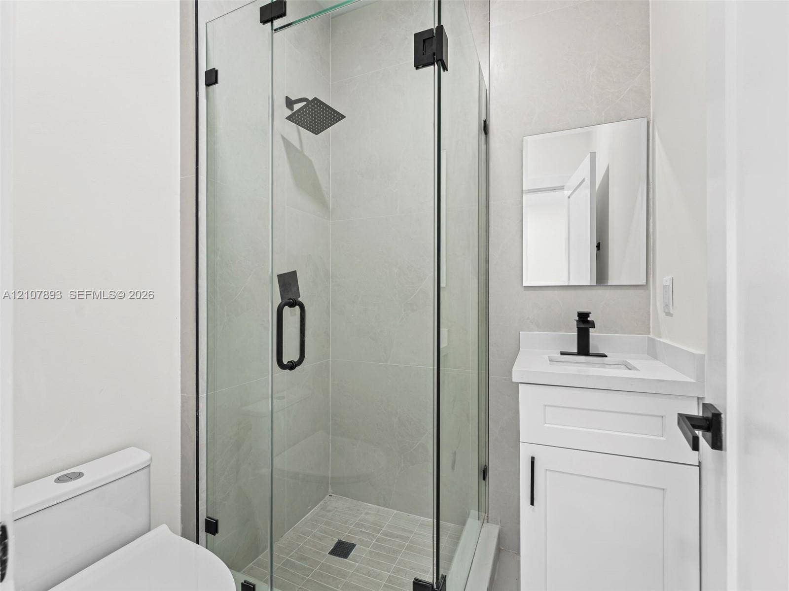 610 NE 164th Terrace, Miami, FL 33162 Walk-in shower with a glass enclosure, square rain-style shower head, white vanity cabinet with stone-finish countertop, square undermount sink, and matte black hardware