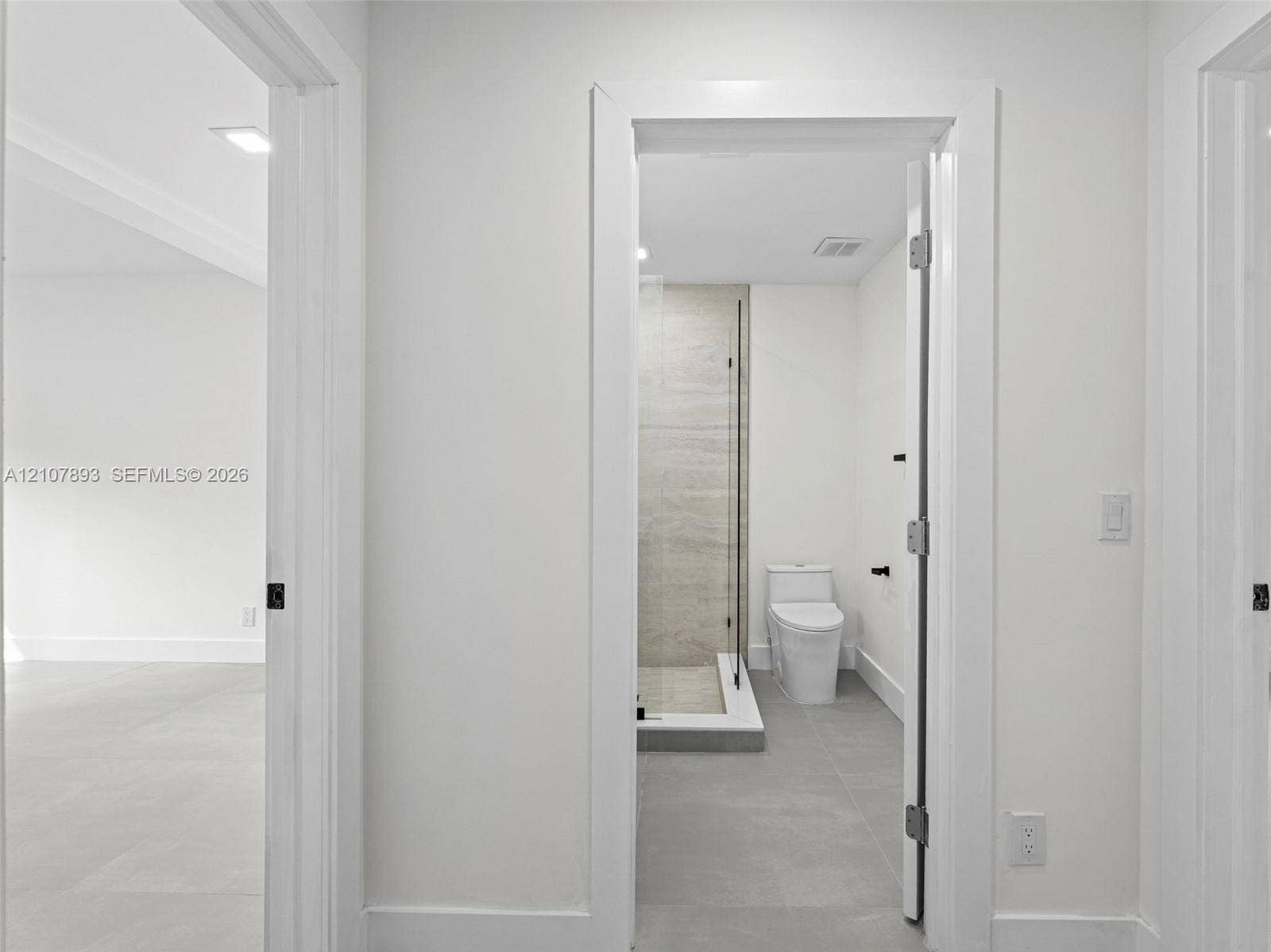 610 NE 164th Terrace, Miami, FL 33162 Bathroom featuring a glass-enclosed shower with large-format wall tile, a two-piece toilet, and grey tile flooring