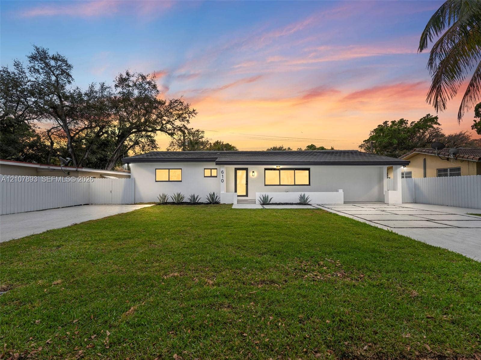 610 NE 164th Terrace, Miami, FL 33162 Single-story residence featuring a smooth stucco exterior, low-pitch roofline, paver driveway with decorative grass inlays, manicured lawn, and perimeter privacy fencing