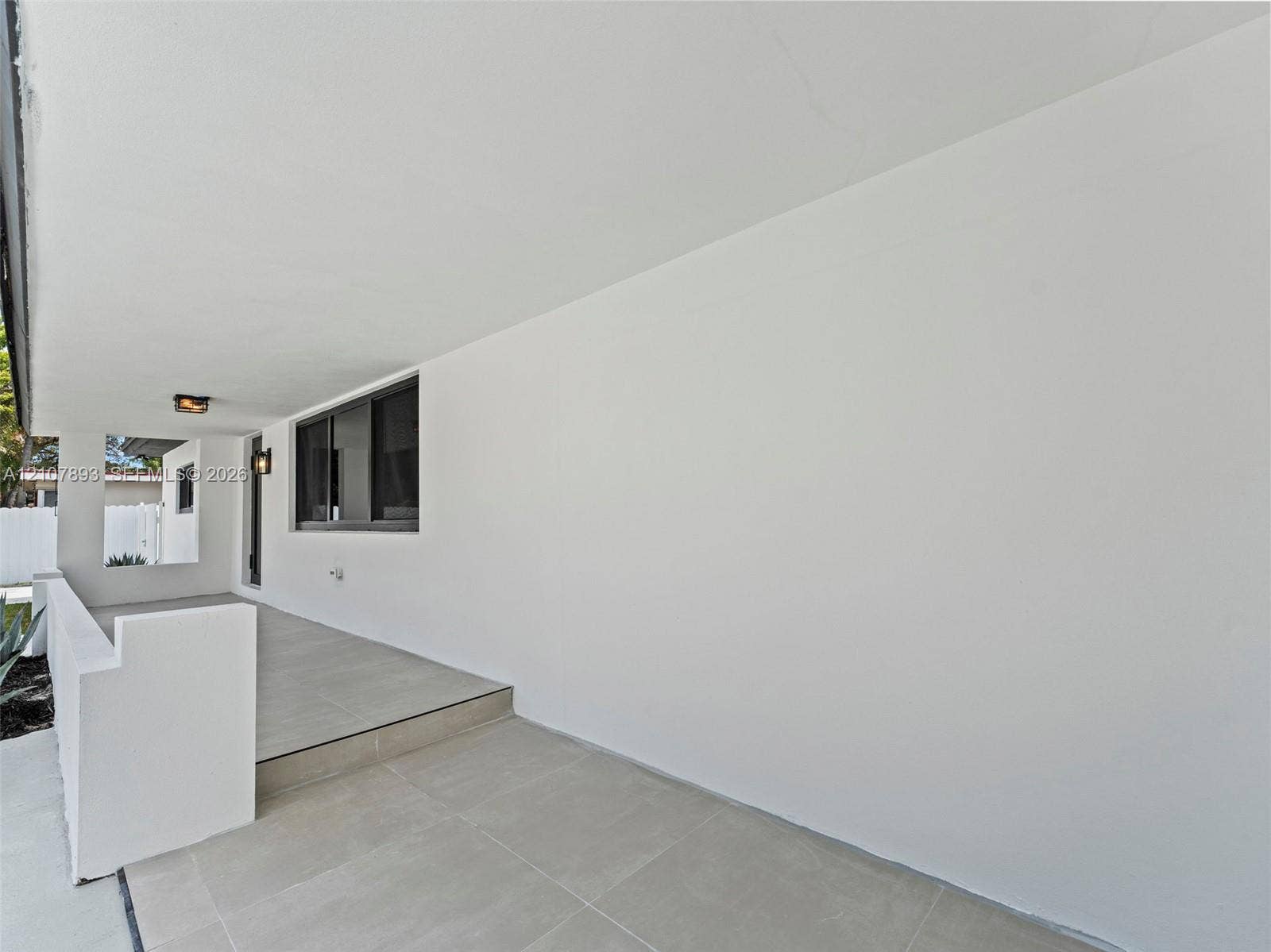610 NE 164th Terrace, Miami, FL 33162 Covered porch featuring large-format tile flooring, a solid masonry partition wall, and wall-mounted exterior lighting fixtures