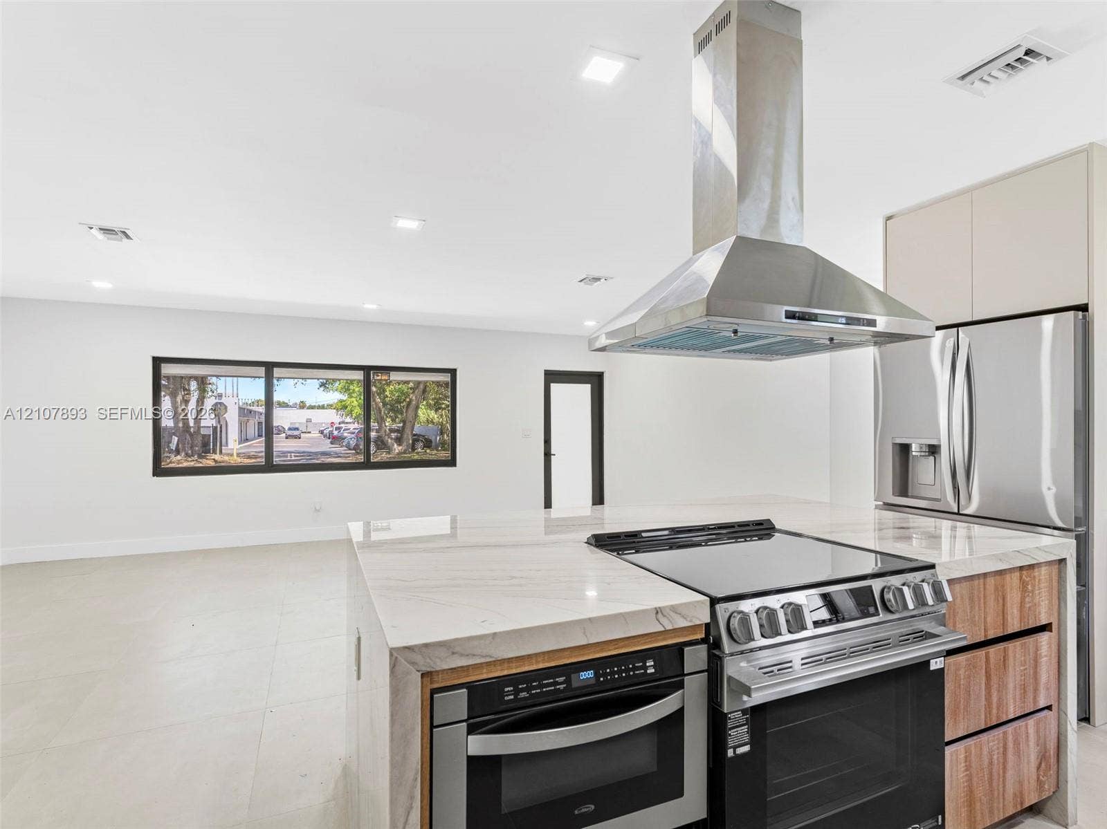 610 NE 164th Terrace, Miami, FL 33162 Kitchen featuring an island with a waterfall-edge countertop, stainless steel range hood, integrated built-in oven, and wood-finish cabinetry