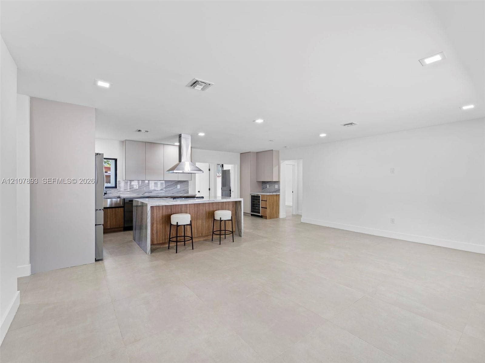 610 NE 164th Terrace, Miami, FL 33162 Open-concept kitchen featuring an oversized island with stone-finish waterfall edges, stainless steel range hood, built-in wine cooler, flat-panel cabinetry, and large-format tile flooring