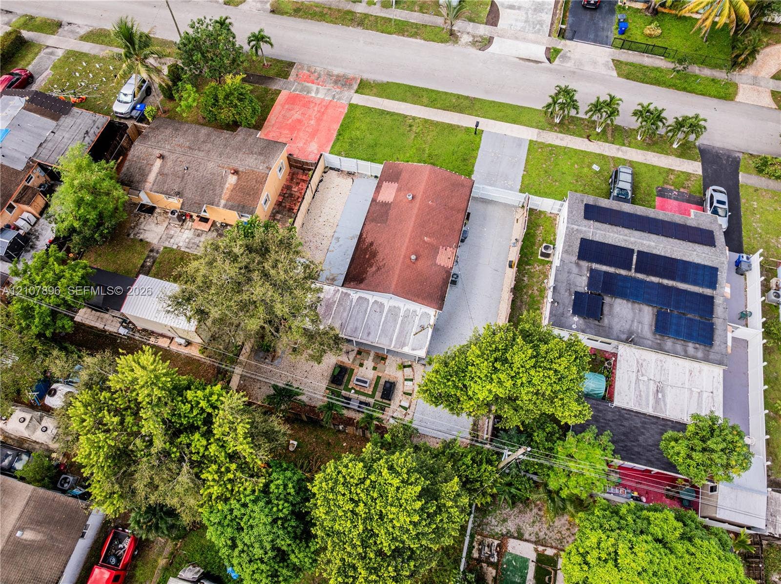 Aerial view featuring a shingle-roof residence, solar panel array, concrete driveway, and mature landscaping