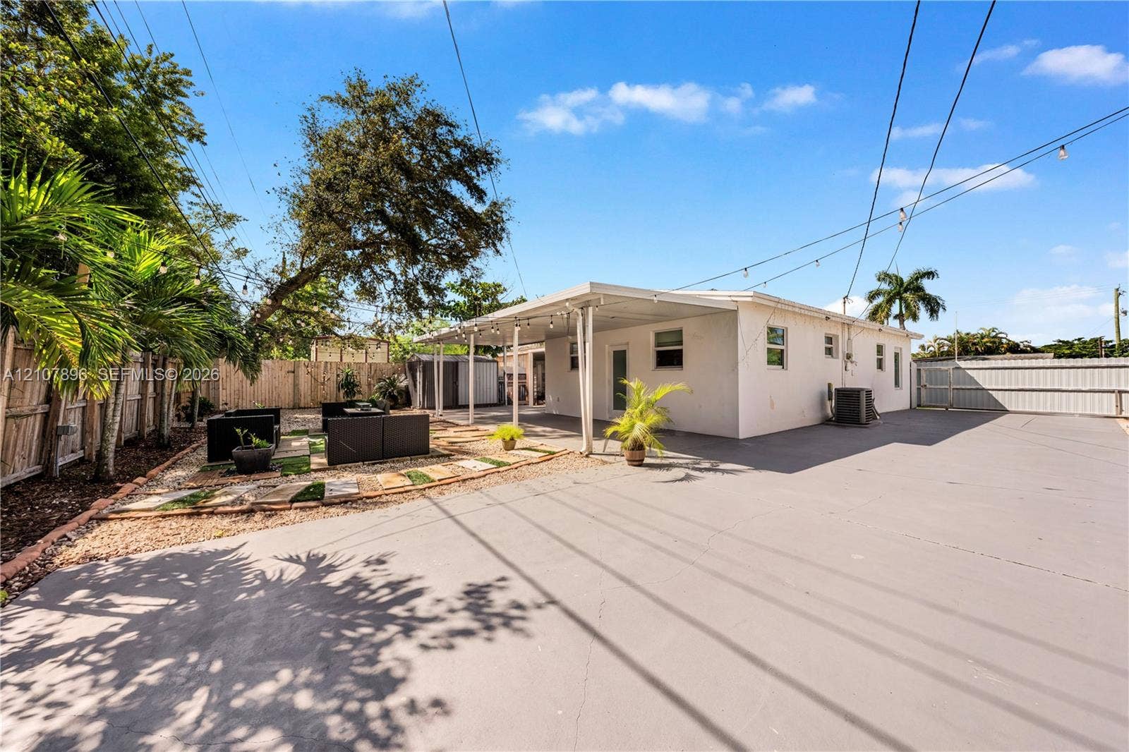 Expansive paved backyard with a covered patio area, perimeter fencing, and established palm trees