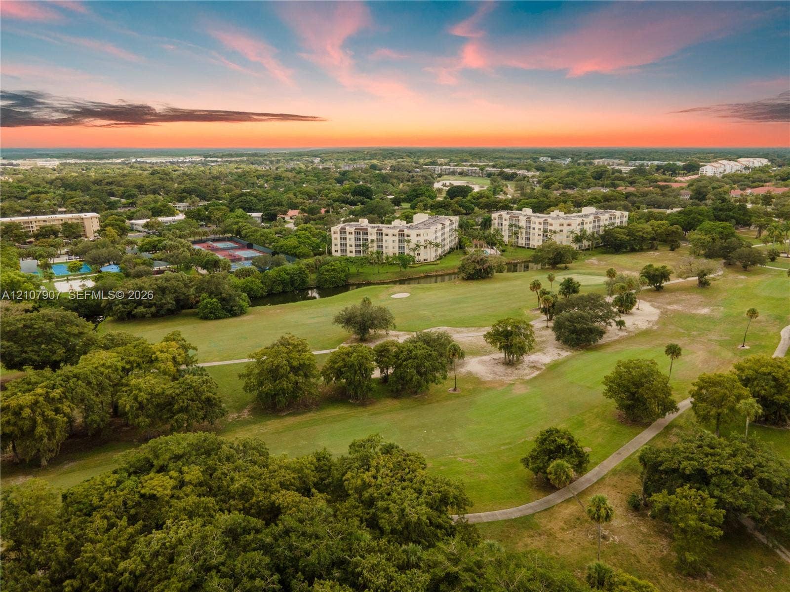 Aerial perspective of a golf course landscape featuring expansive fairways, mature tree canopy, integrated water features, and paved cart paths