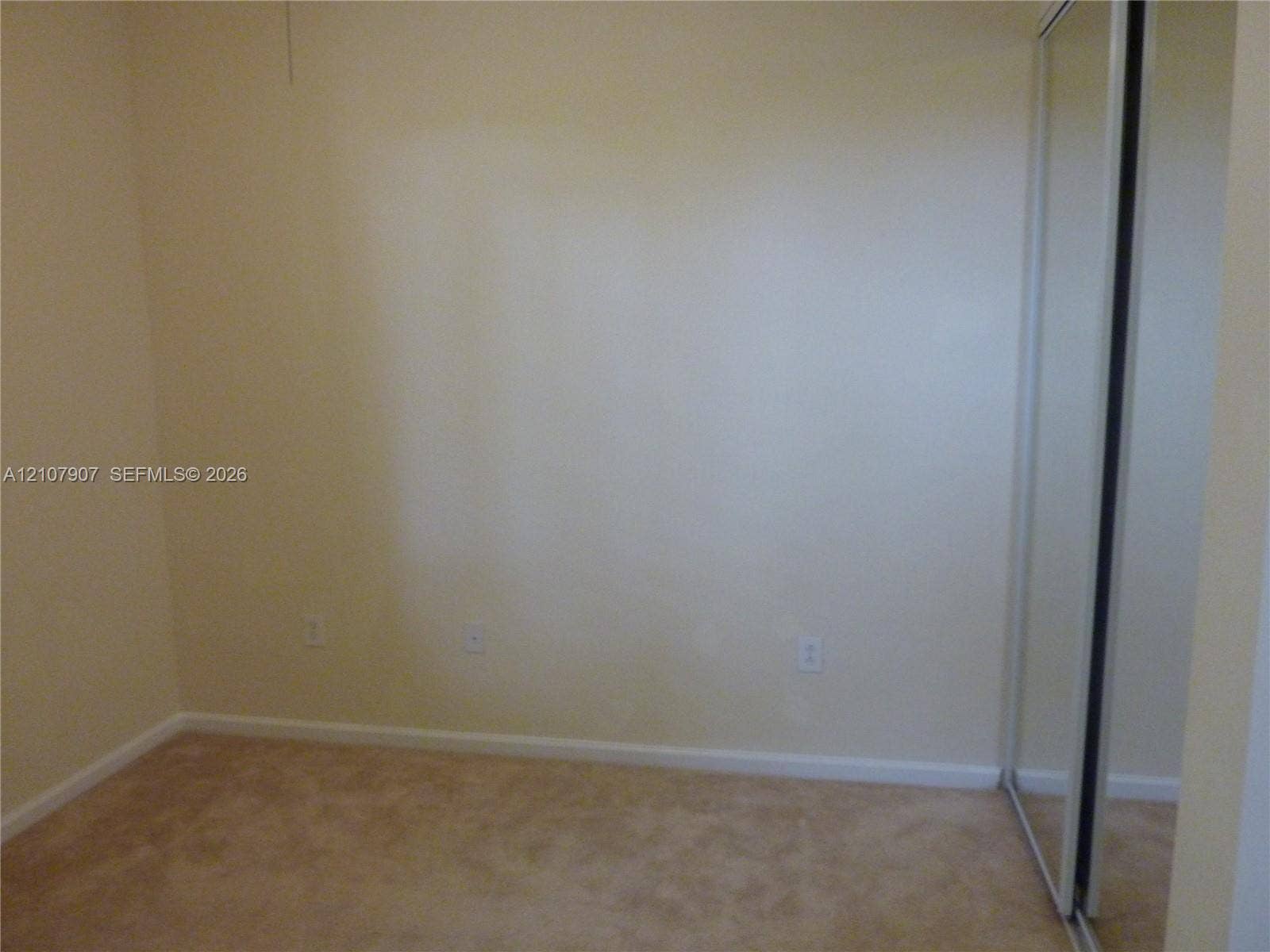 Neutral-toned interior space featuring wall-to-wall carpeting and a floor-to-ceiling mirrored sliding-door closet