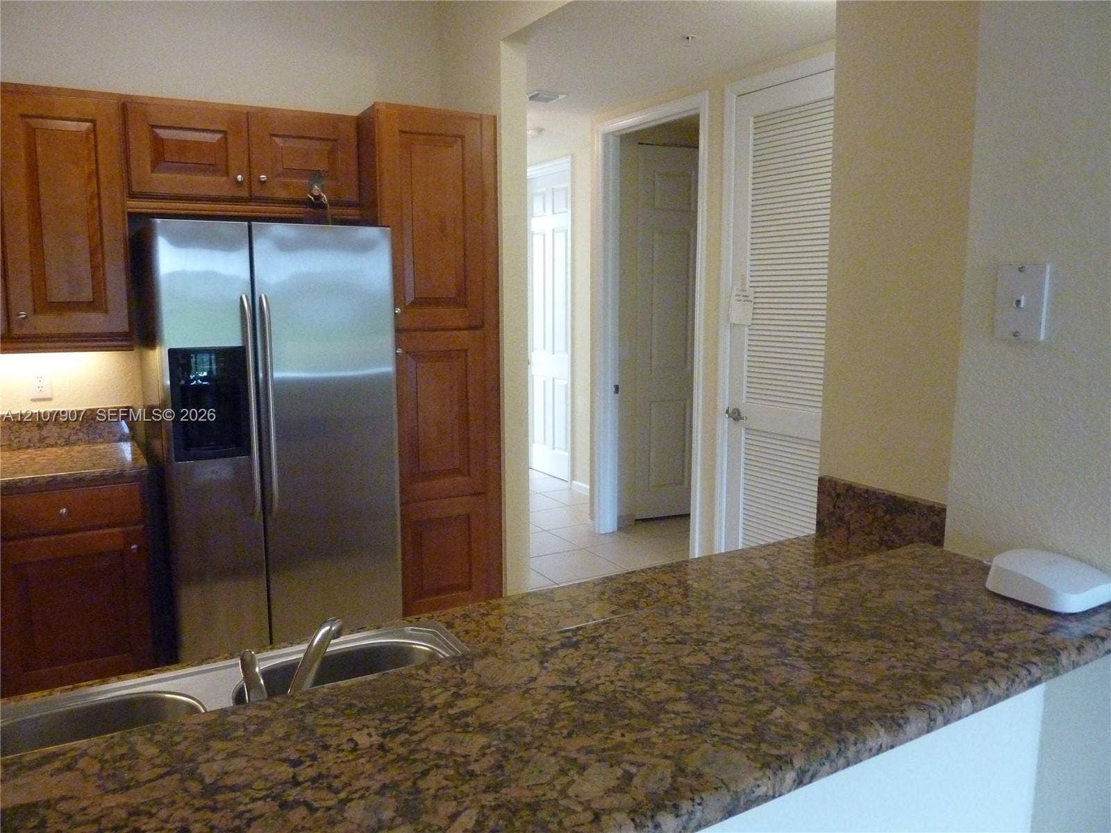 Kitchen featuring natural finish wood cabinetry, stone-surface countertops, dual-basin stainless steel sink, and stainless steel refrigerator