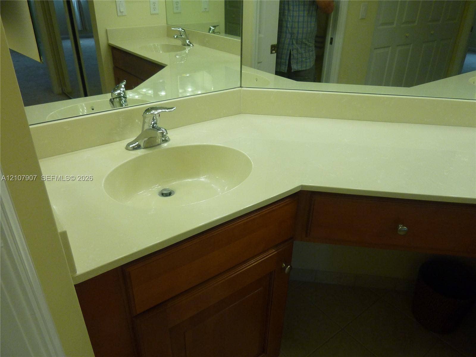 Vanity featuring a solid-surface countertop with an integrated oval sink, chrome-finish faucet, wood-finish cabinetry, and a full-width wall mirror