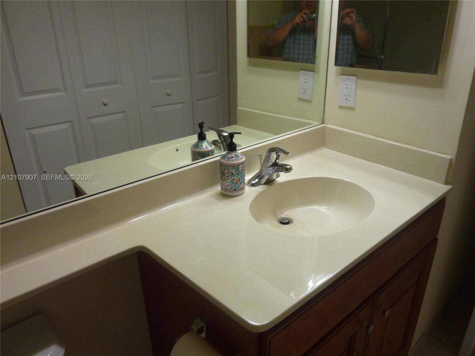 Vanity featuring an integrated molded sink, solid-surface countertop, wood-finish cabinetry, and a full-width wall mirror
