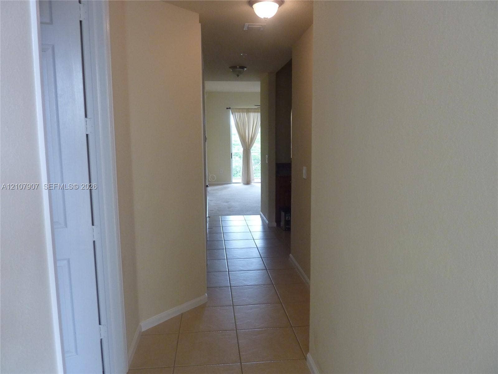 Neutral-toned interior hallway featuring large-format ceramic tile flooring, two ceiling-mounted light fixtures, and a multi-panel door
