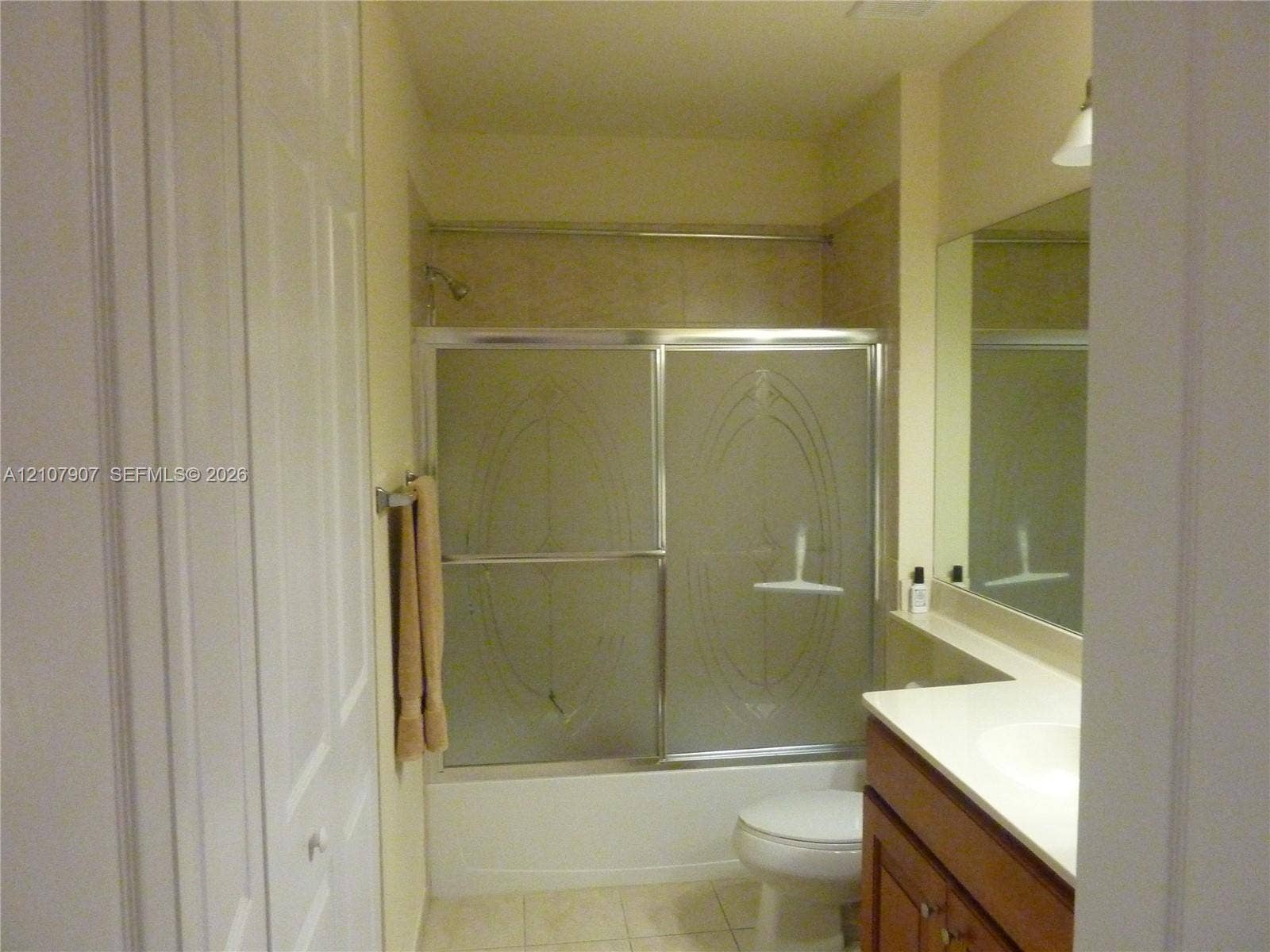 Bathroom featuring a shower-tub combination with etched glass sliding doors, wood-finish vanity cabinetry, a solid surface countertop, and a wall-to-wall mirror