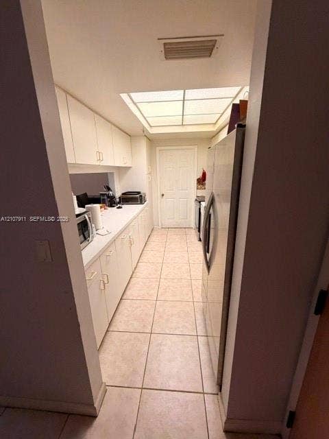 9755 NW 52nd Street, #218, Doral, FL 33178 Galley kitchen featuring white cabinetry, light-toned tiled flooring, a skylight, and a stainless steel refrigerator