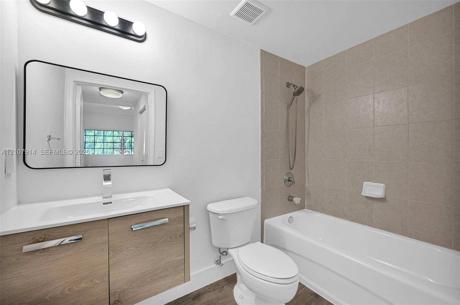 7340 NW 114th Avenue, #205, Doral, FL 33178 Floating wood-finish vanity with an integrated sink, rectangular mirror with a black frame, and a shower-tub combination featuring square tile surround and a handheld showerhead