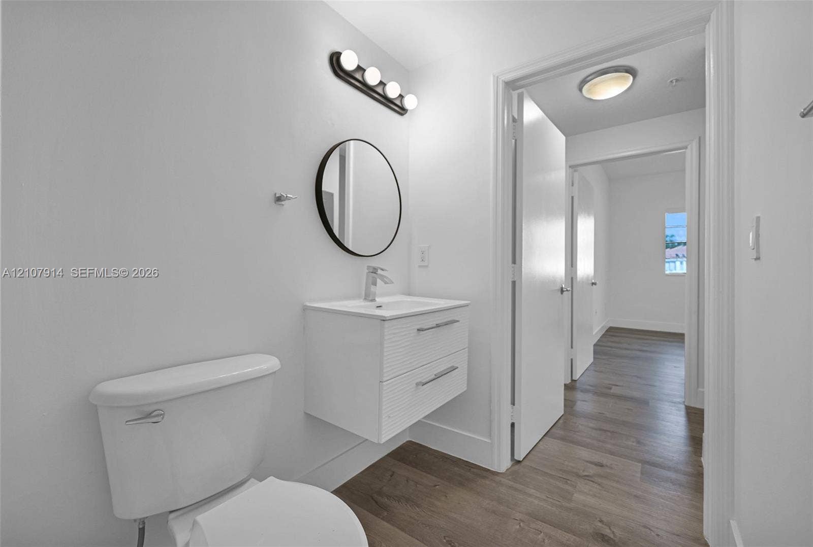 7340 NW 114th Avenue, #205, Doral, FL 33178 Floating white vanity with double drawers, round mirror, four-light matte black vanity fixture, and wood-finish flooring