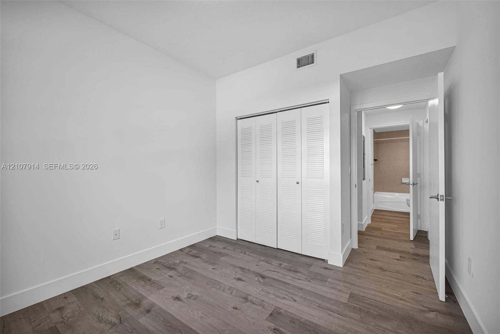 7340 NW 114th Avenue, #205, Doral, FL 33178 Room featuring wood-finish flooring, white walls, and a built-in double-door closet with louvered panels