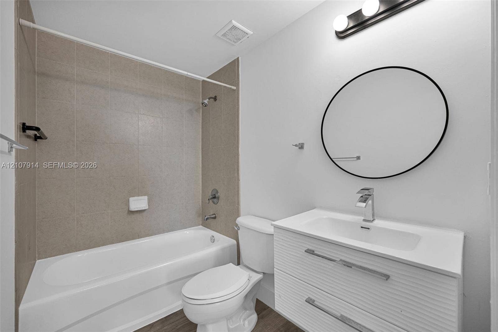 7340 NW 114th Avenue, #205, Doral, FL 33178 Modern bathroom featuring a floating vanity with a white countertop, circular wall-mounted mirror, three-light fixture, and bathtub with neutral wall tile