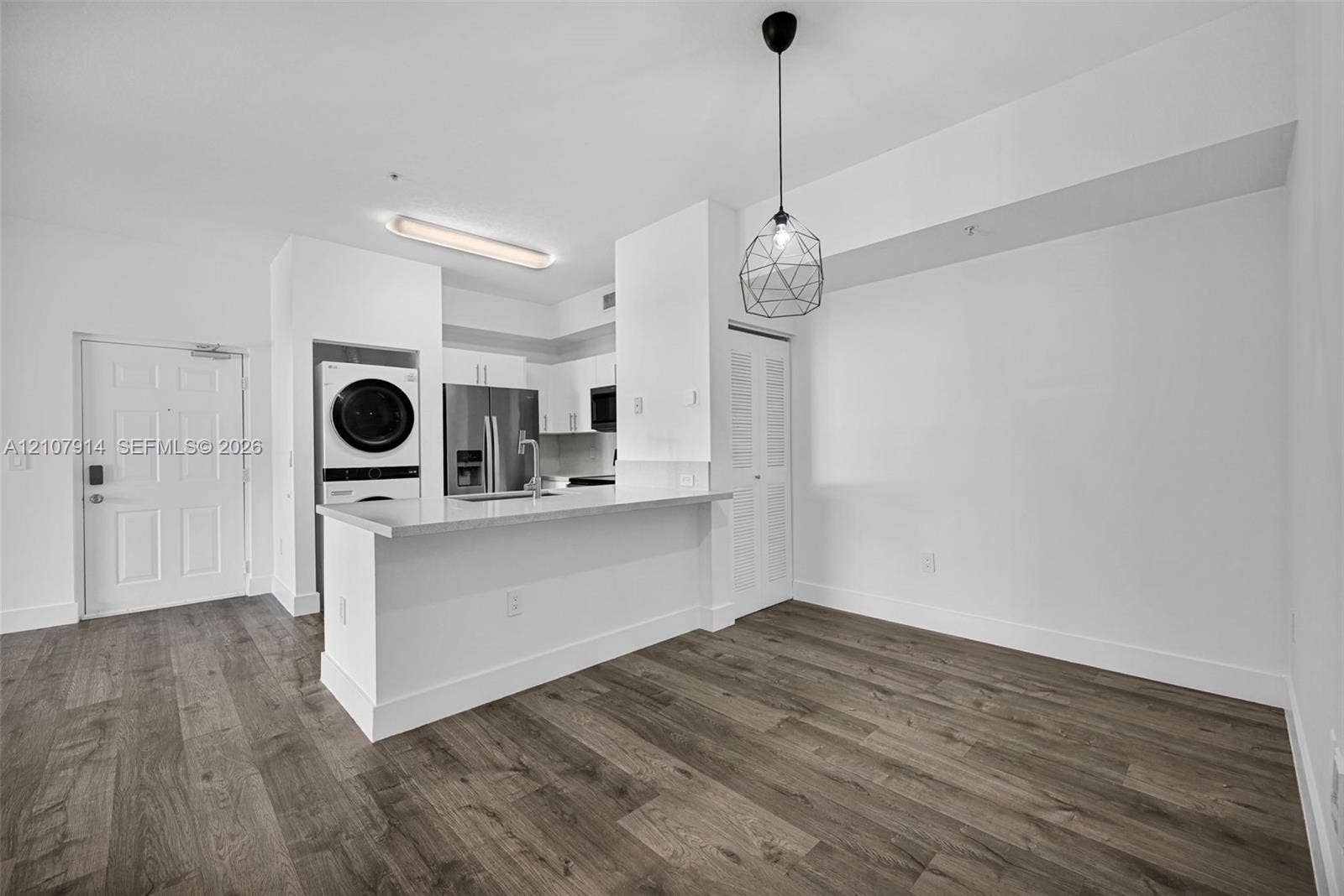 7340 NW 114th Avenue, #205, Doral, FL 33178 Kitchen featuring a breakfast bar with stone-surfaced countertop, stainless steel refrigerator, integrated laundry center, wood-finish flooring, and geometric pendant lighting