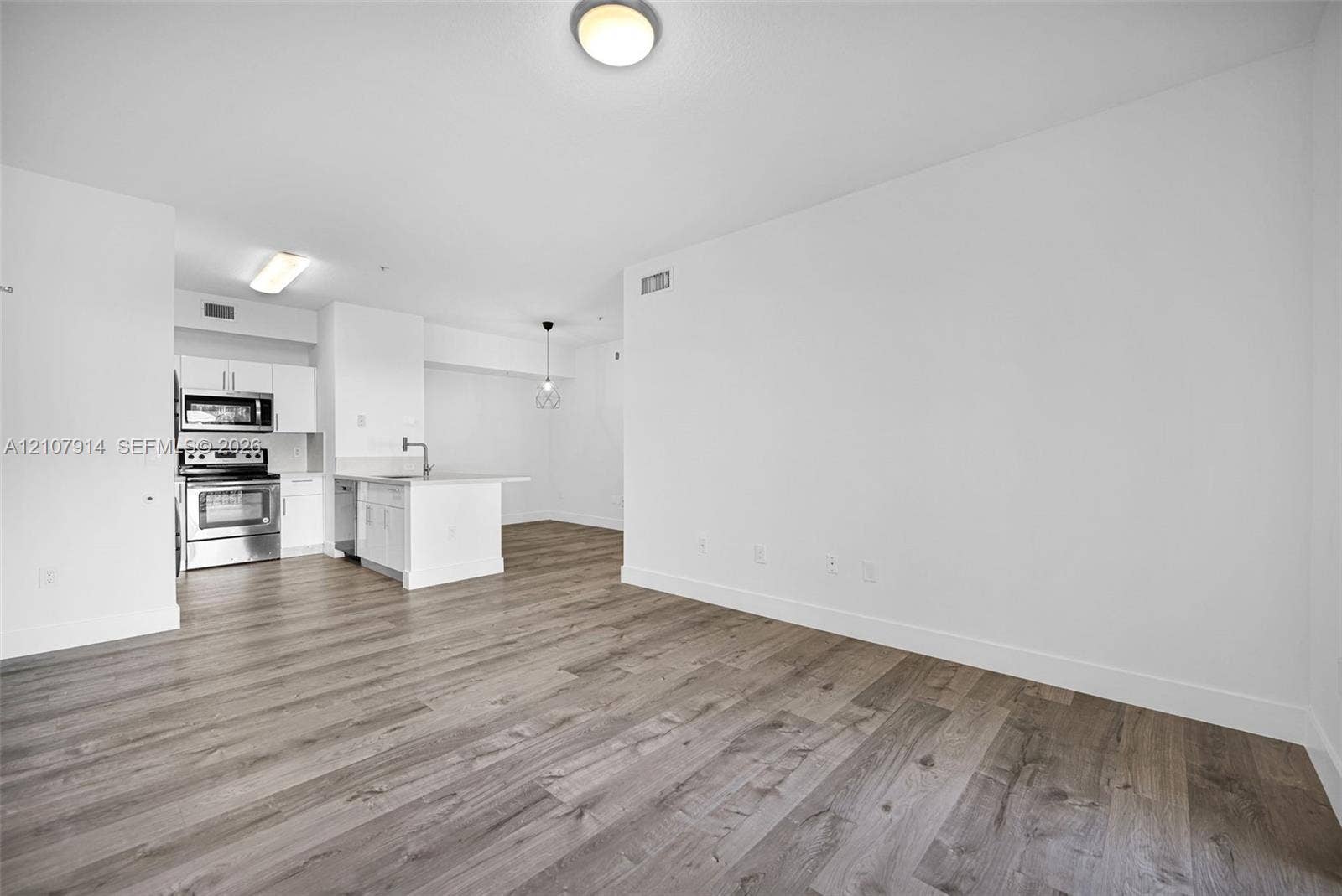 7340 NW 114th Avenue, #205, Doral, FL 33178 Open-concept interior featuring wood-finish flooring, white cabinetry, stainless steel appliances, and ceiling-mounted lighting fixtures