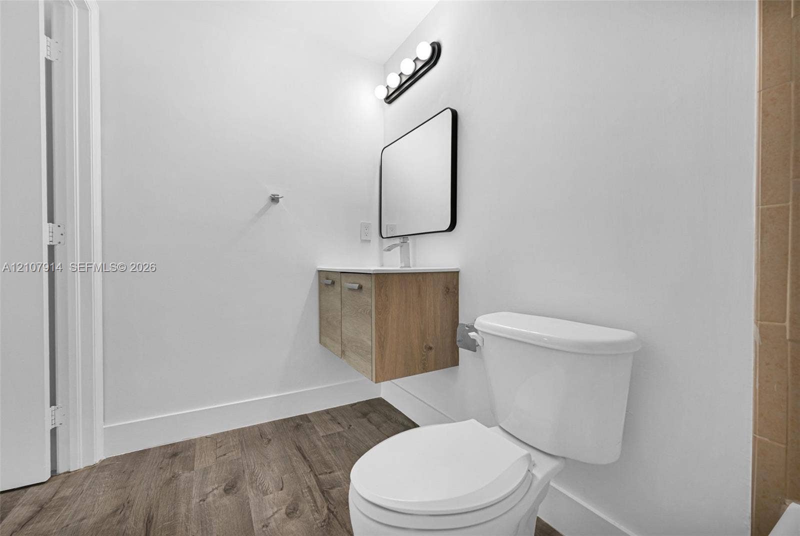 7340 NW 114th Avenue, #205, Doral, FL 33178 Floating wood-finish vanity with countertop, rectangular mirror with black frame, four-light vanity fixture, and wood-finish flooring