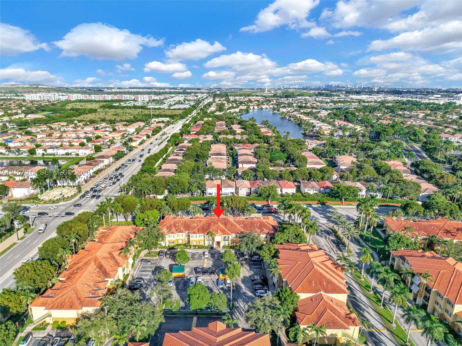 7340 NW 114th Avenue, #205, Doral, FL 33178 Aerial perspective of a multi-story residential building featuring terracotta tile roofing, stucco exterior, and a dedicated surface parking area surrounded by palm trees and mature landscaping