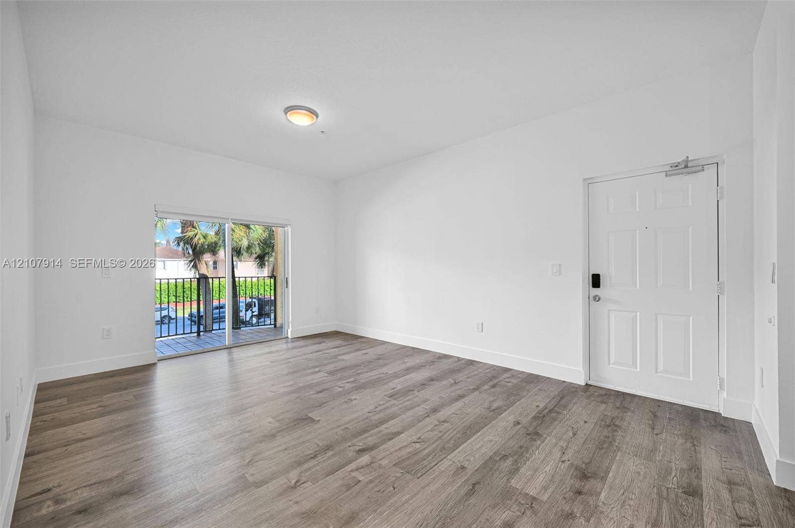 7340 NW 114th Avenue, #205, Doral, FL 33178 Open-concept interior featuring wood-finish flooring, white walls, flush-mount ceiling lighting, a multi-panel entry door, and sliding glass doors to a balcony with metal railing