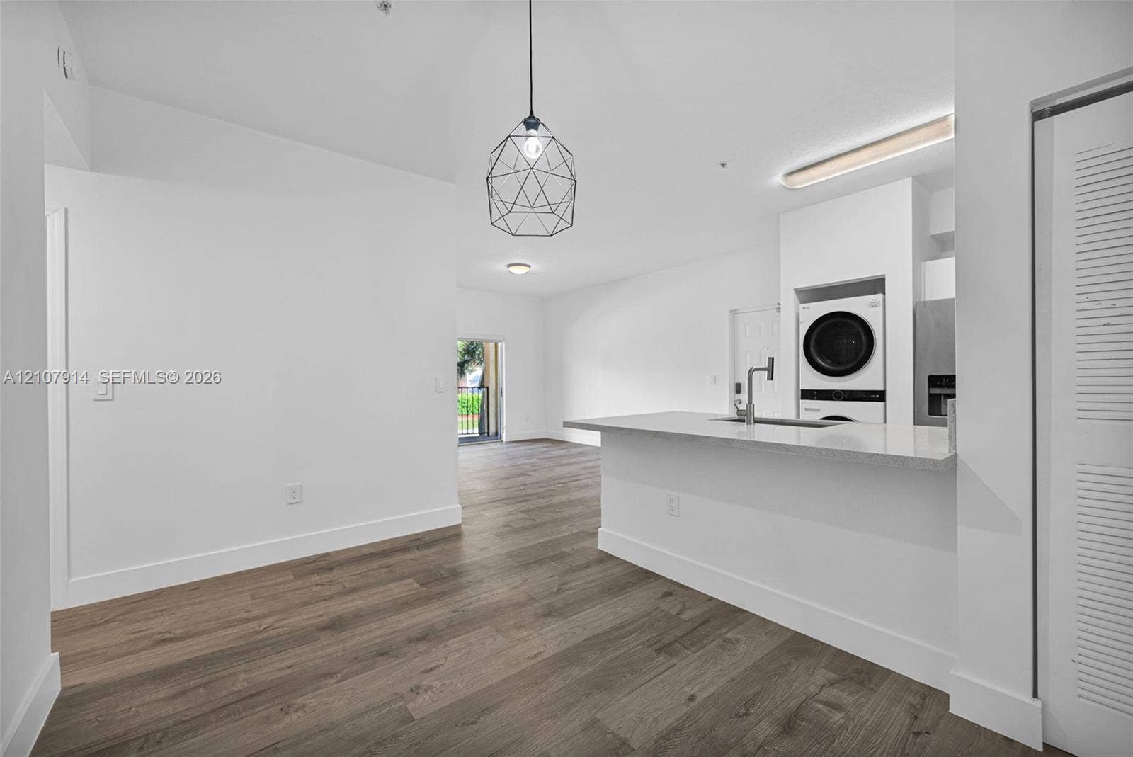 7340 NW 114th Avenue, #205, Doral, FL 33178 Kitchen featuring a quartz countertop island with an integrated sink, geometric pendant lighting, wood-finish flooring, and built-in stacked laundry appliances