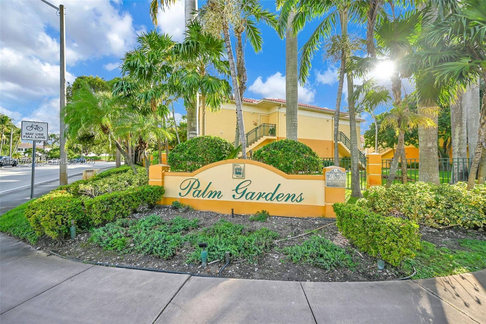 7340 NW 114th Avenue, #205, Doral, FL 33178 Stucco exterior community signage featuring masonry pillar accents, decorative landscaping, and mature palm trees