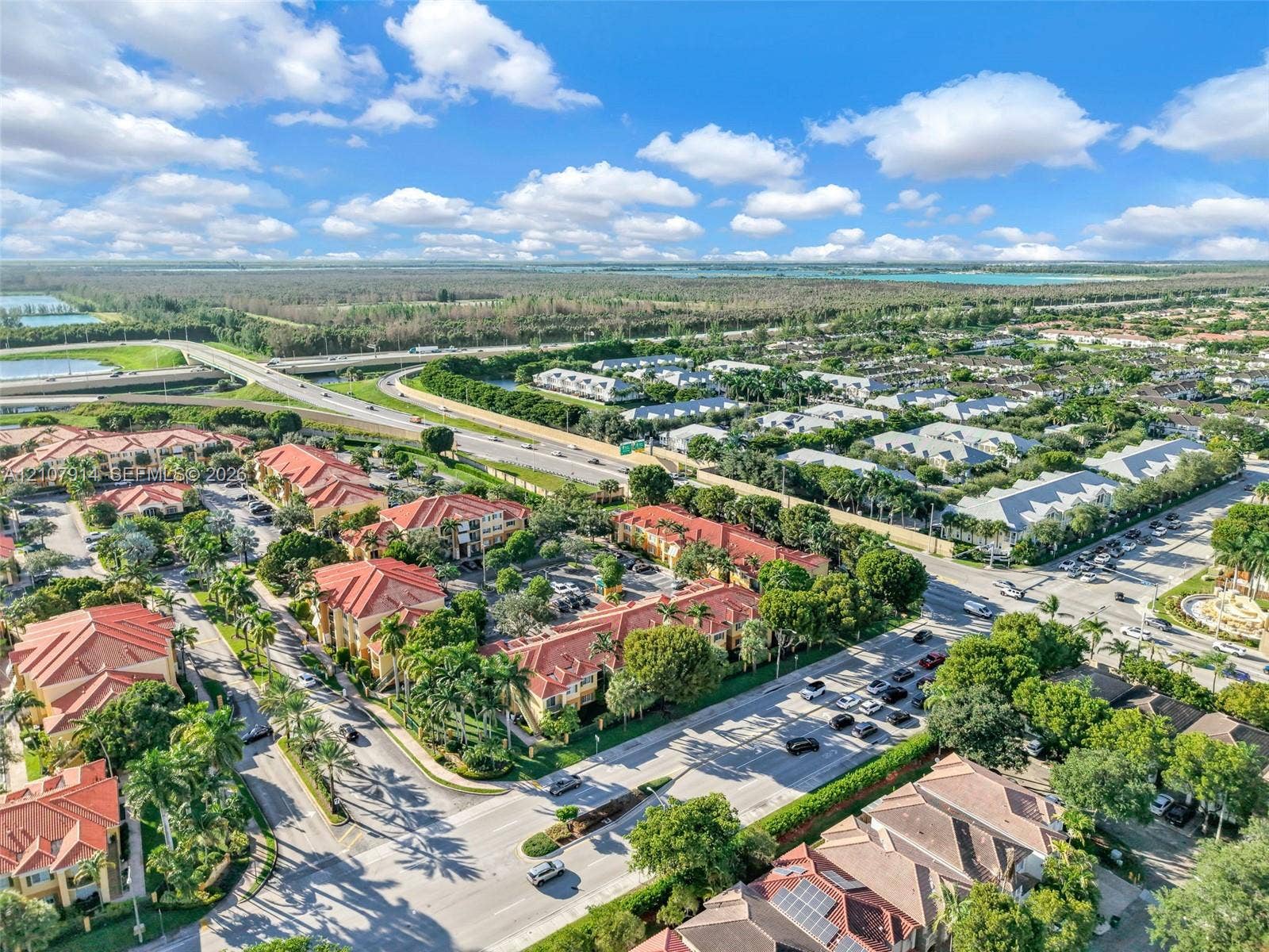 7340 NW 114th Avenue, #205, Doral, FL 33178 Aerial perspective of a multi-building residential development featuring terracotta-style tile roofs, mature canopy trees, paved thoroughfares, and manicured landscaping