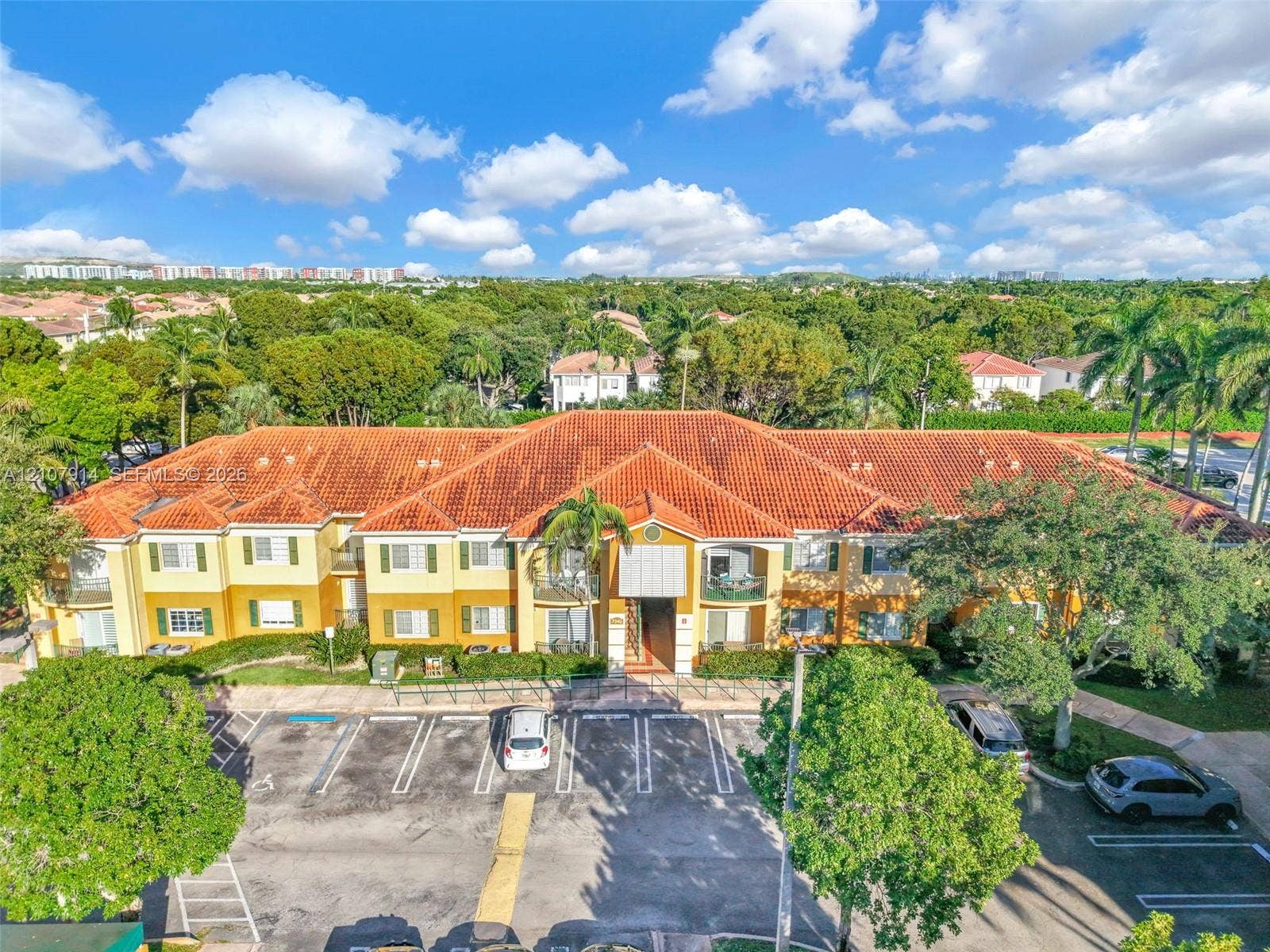7340 NW 114th Avenue, #205, Doral, FL 33178 Low-rise multi-unit residential building featuring a barrel tile roof, stucco exterior, decorative shutters, and paved surface parking