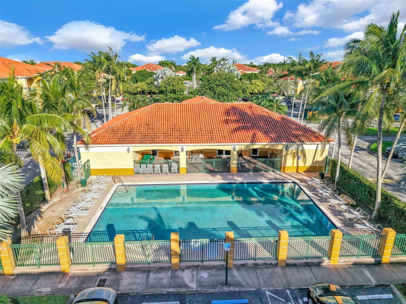 7340 NW 114th Avenue, #205, Doral, FL 33178 Community swimming pool featuring a rectangular basin, perimeter metal fencing, masonry pillars, and a covered pavilion with a terracotta tile roof, surrounded by mature palm trees
