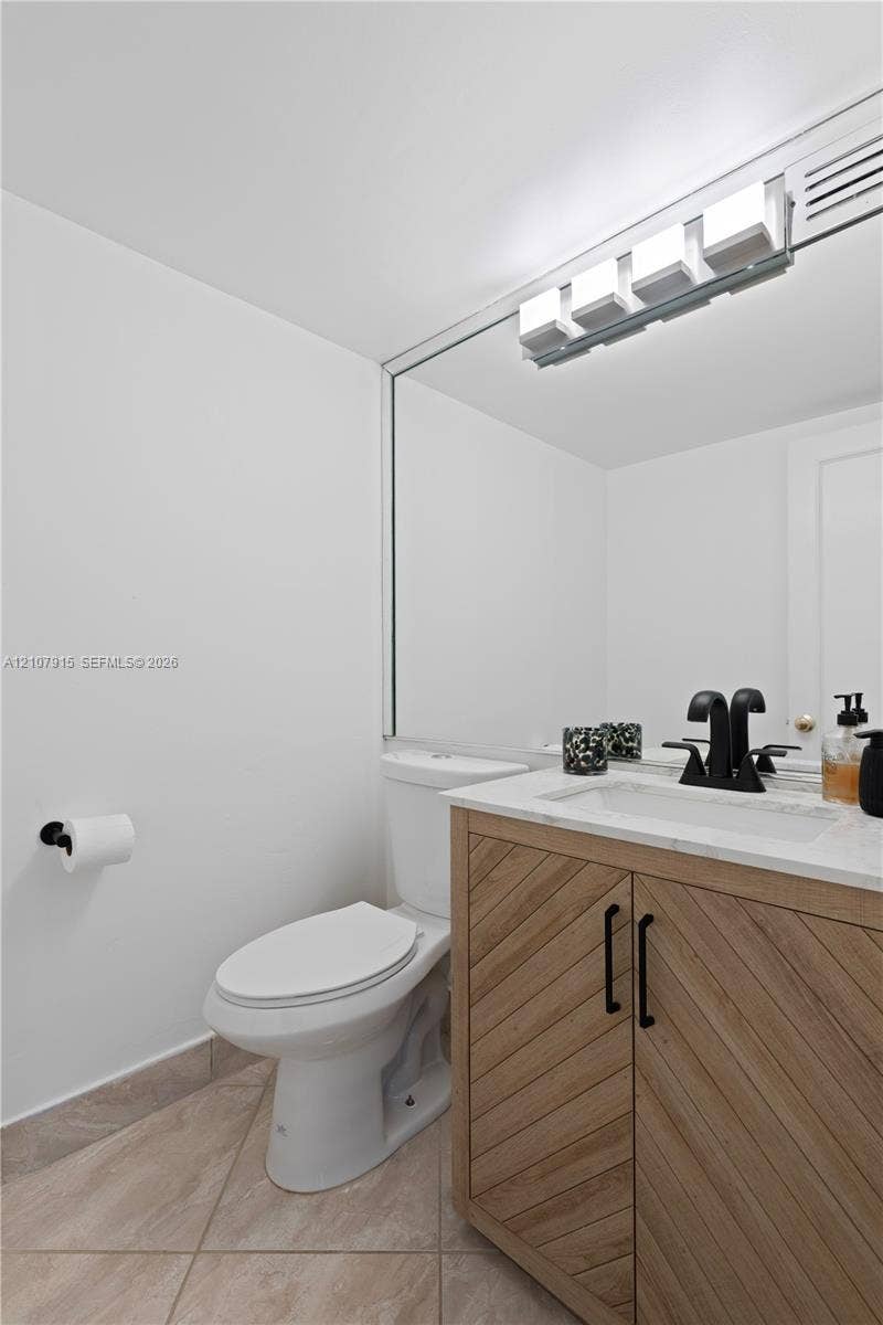 400 Leslie Drive, #622, Hallandale Beach, Hallandale Beach, FL 33009 Vanity featuring wood-grain cabinet doors in a chevron pattern, light-toned stone countertop, integrated sink, matte black hardware, and an expansive wall-mounted mirror