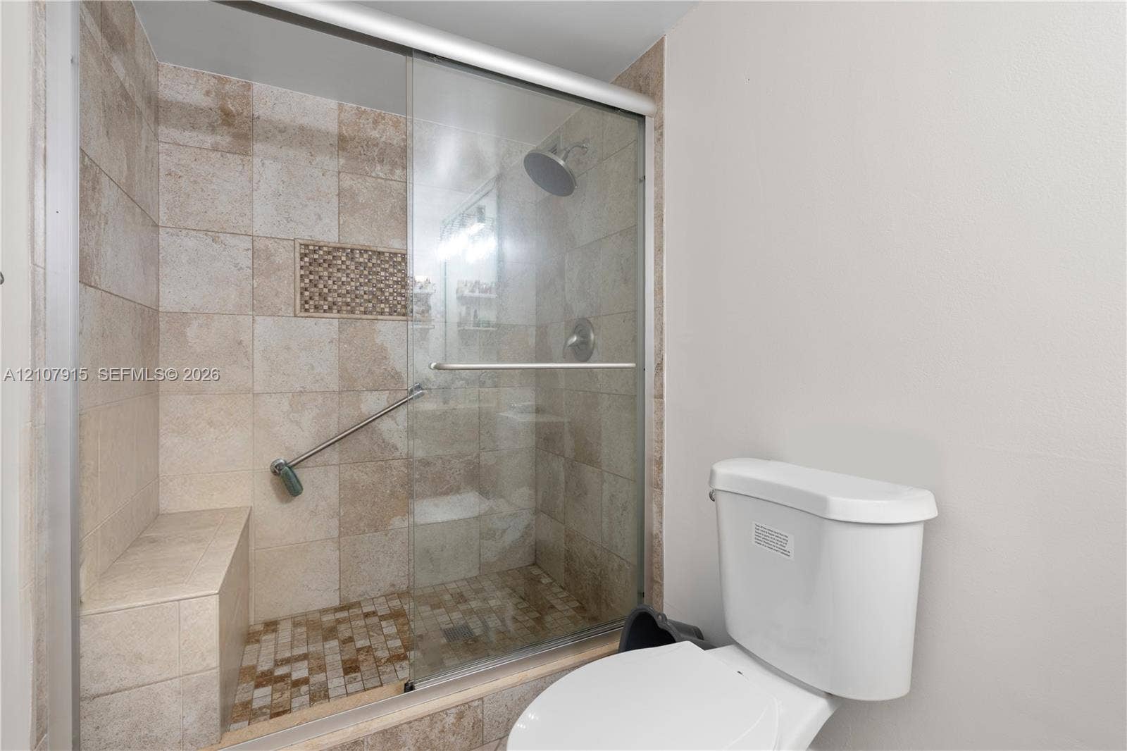400 Leslie Drive, #622, Hallandale Beach, Hallandale Beach, FL 33009 Walk-in shower featuring tile walls, a built-in bench, a decorative mosaic tile inset, a glass sliding door, and a wall-mounted shower head