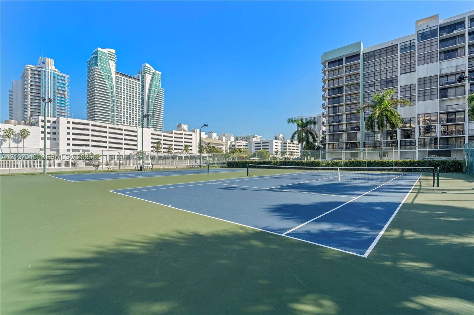 400 Leslie Drive, #622, Hallandale Beach, Hallandale Beach, FL 33009 Dual hard-court tennis facility featuring blue and green surfacing, perimeter chain-link fencing, and pole-mounted lighting