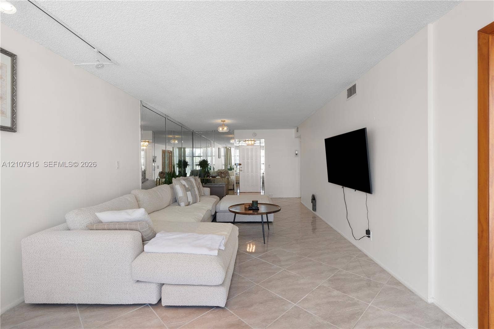 400 Leslie Drive, #622, Hallandale Beach, Hallandale Beach, FL 33009 Spacious room featuring neutral tile flooring laid on a diagonal, full-height wall-mounted mirror paneling, textured ceiling, and track lighting