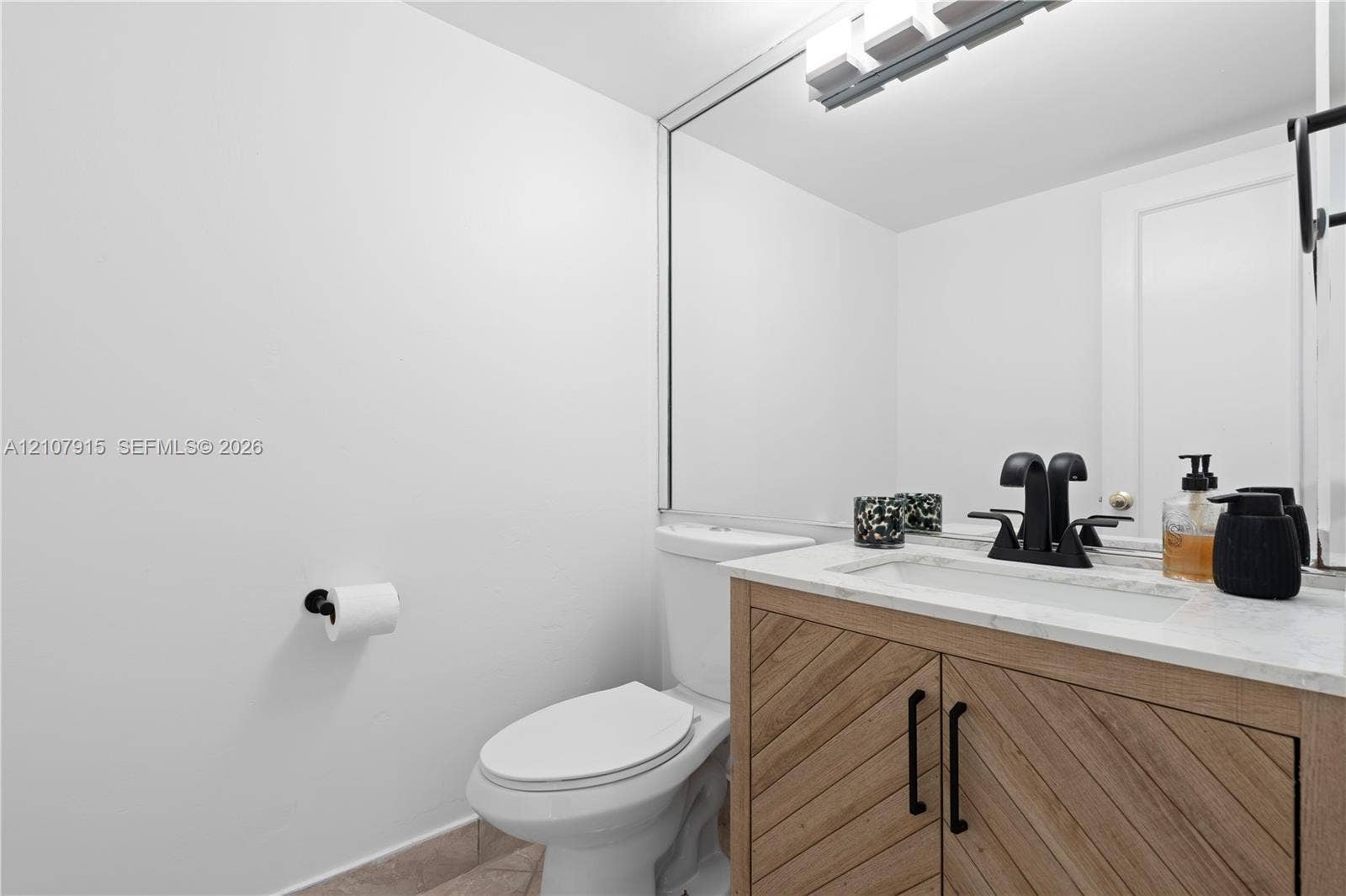 400 Leslie Drive, #622, Hallandale Beach, Hallandale Beach, FL 33009 Bathroom vanity with wood-finish cabinetry featuring a diagonal grain pattern, stone-top counter with an integrated basin, matte black faucet hardware, and a full-width wall mirror