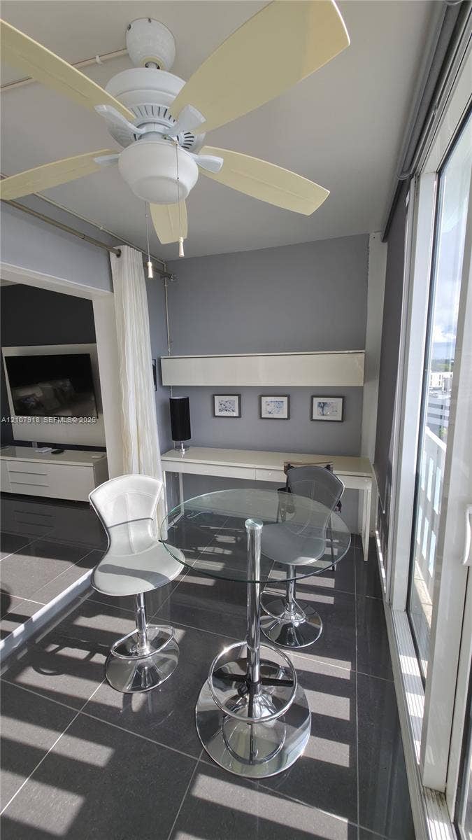 Dark tile flooring, ceiling fan with integrated lighting, and built-in wall-mounted desk with overhead storage cabinet