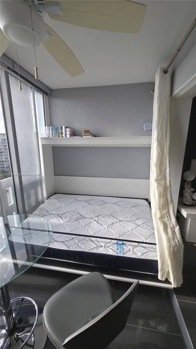 Built-in wall unit featuring an integrated shelf, large windows with floor-to-ceiling glass, polished tile flooring, and a ceiling-mounted light fixture with a fan