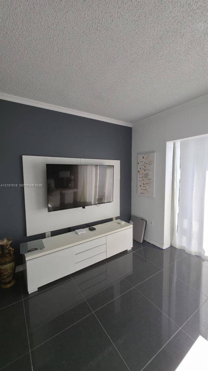 Large-format gray tile flooring, accent wall with built-in white media console, and white crown molding