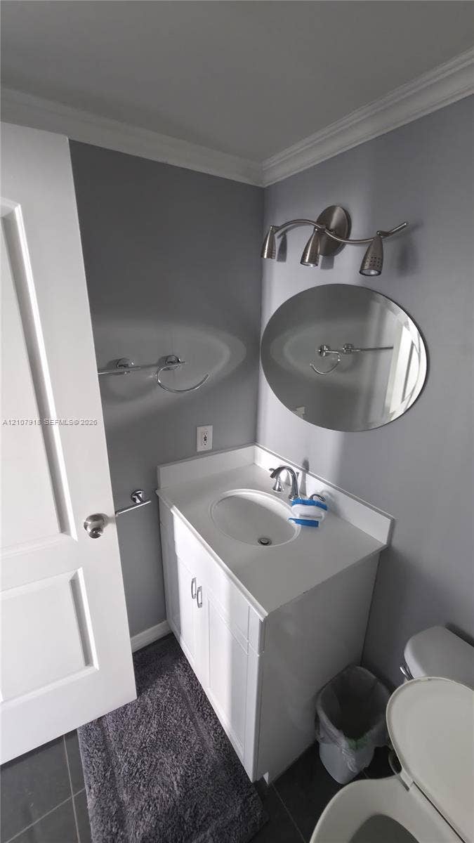 White vanity with an integrated countertop and basin, oval frameless mirror, and brushed-finish three-light vanity fixture